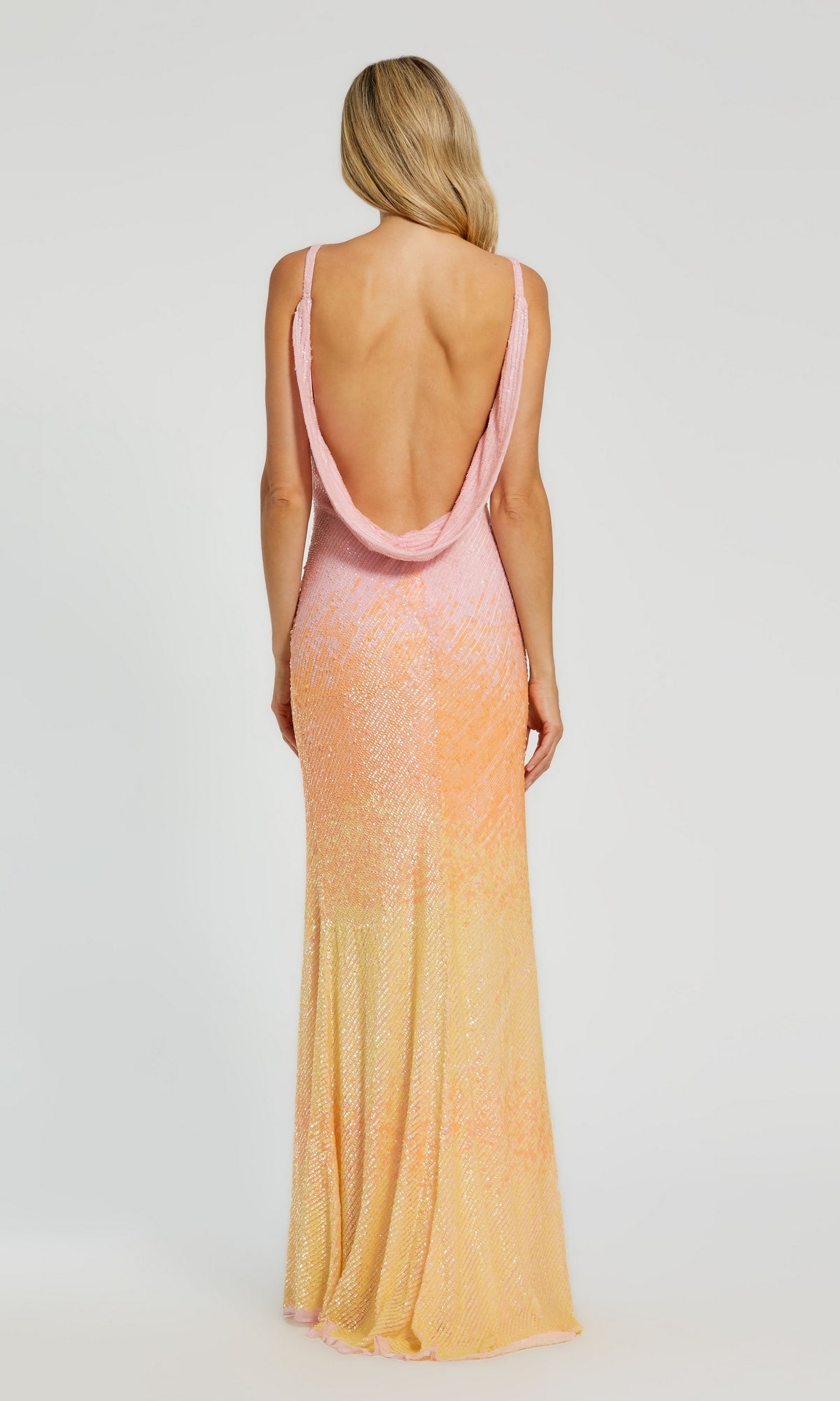 A woman with long blonde hair wears the Long Formal Dress 5763 by Mac Duggal—a sleeveless, ombre sunset gown with a cowl open back in gradient pink, orange, and yellow—standing against a plain background.